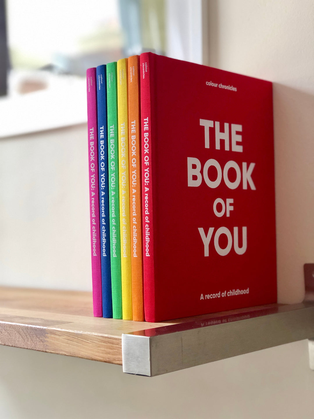 Book of You childhood memory journals on a shelf in six rainbow colours